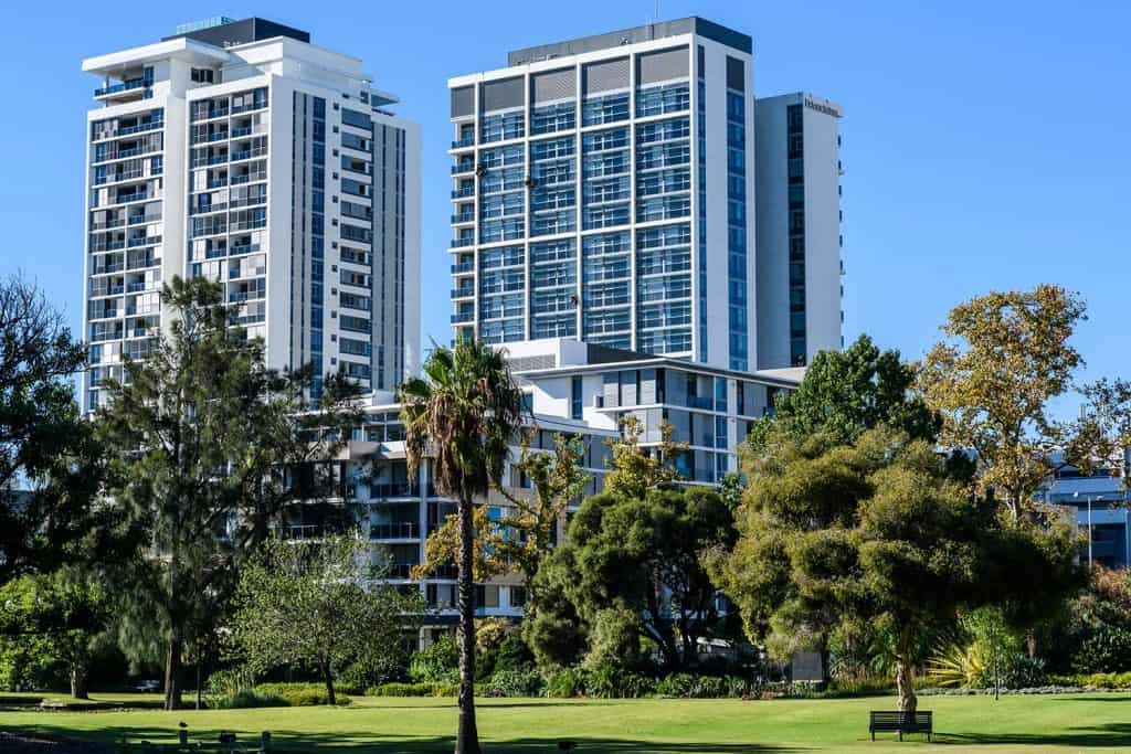Two tall buildings with trees and grass in front of them.