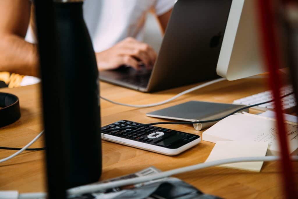 A person sitting at a desk with a laptop and a cell phone.